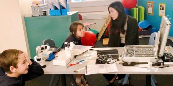 Megan Teh with young students at a desk covered in optical equipment