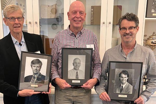three retired optometrists hold up portraits of their younger selves