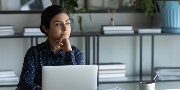 woman at laptop staring into middle distance in thought